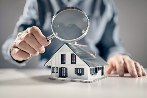 An illustration of a man scrutinizing a model home with a magnifying glass, to illustrate home valuation skills
