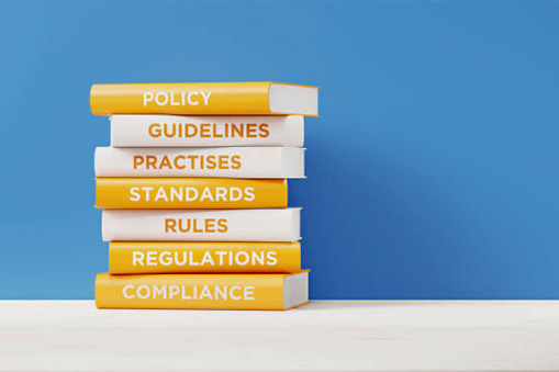 A stack of books with titles like "Guidelines", "Practices", "Standards", "Rules", and "Regulations" to illustrate knowledge of legal requirements
