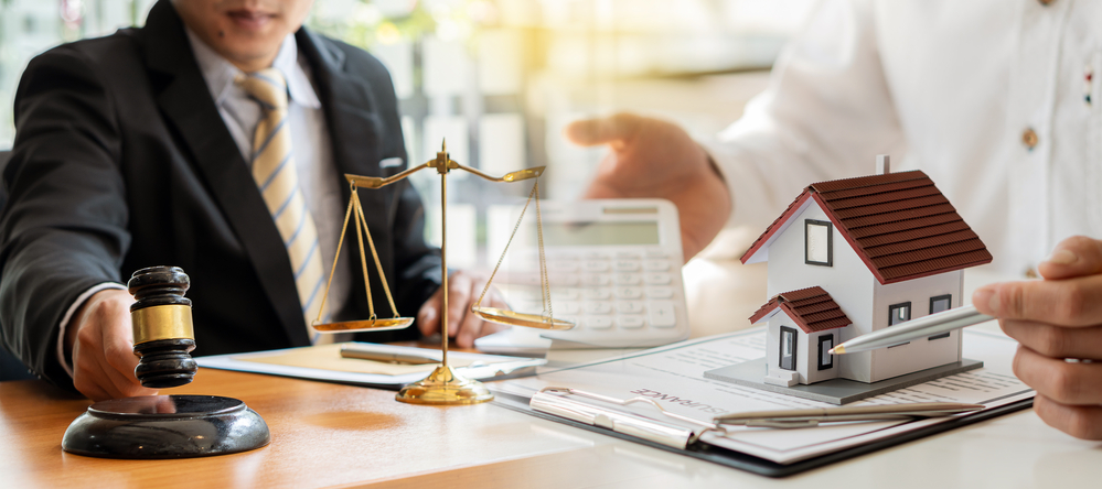 Illustrative photo with people around a meeting table, models of homes, scales of justice, paperwork